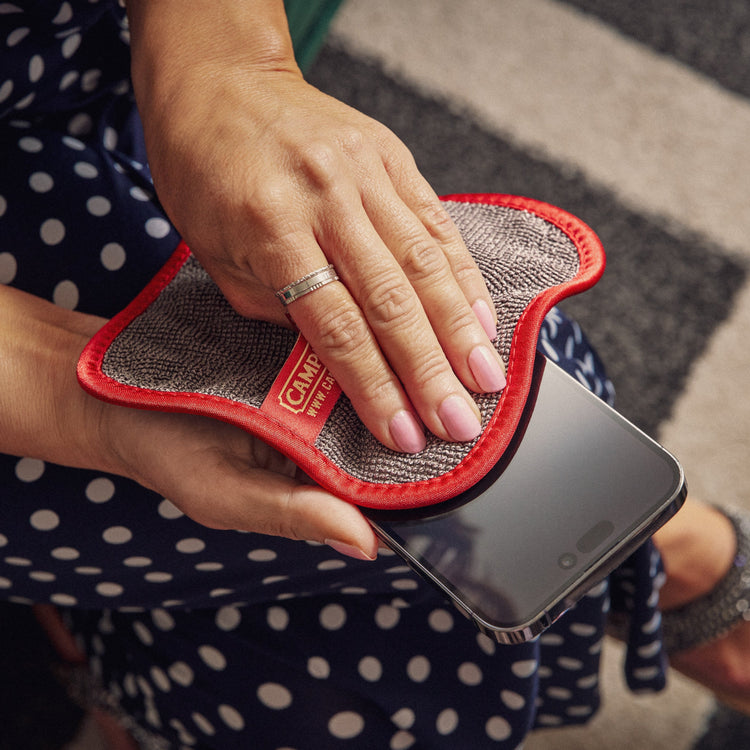 Person cleaning a smartphone with a cloth on a patterned surface