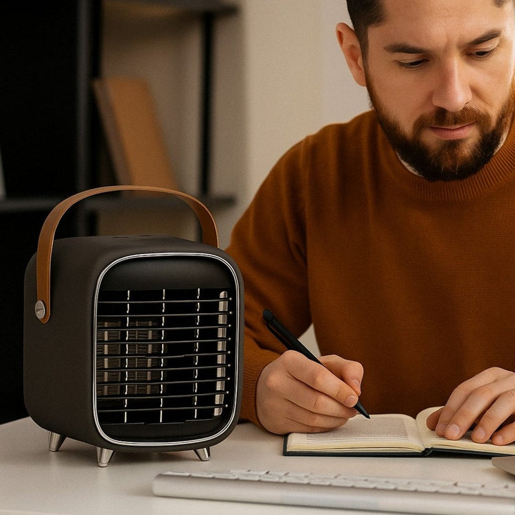 Man sitting at a desk with a laptop, notebook, and small black portable heater.