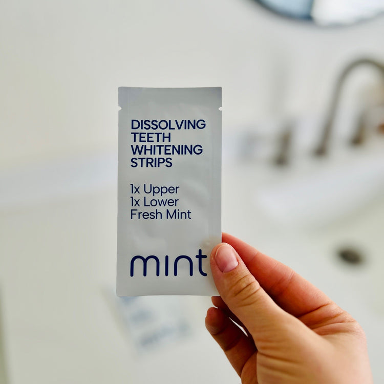 Hand holding a packet of dissolving teeth whitening strips with 'mint' flavor.