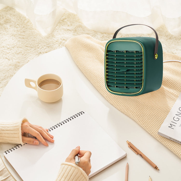 Small green portable heater on a table with a notebook, cup, and pencils.