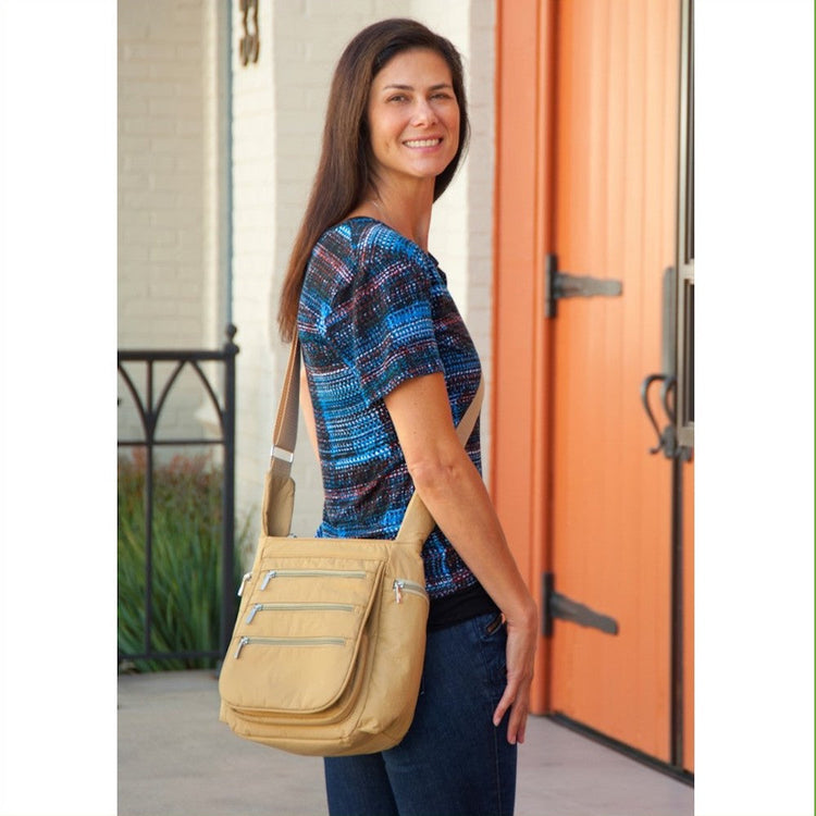 A person smiling and carrying a beige crossbody vegan leather daybag with zippered pockets.