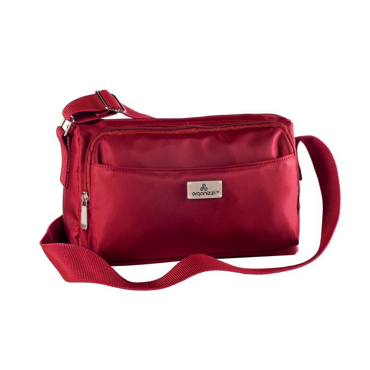 A person seated on a bench with a striped skirt and a black top, wearing a blue crossbody bag with multiple compartments.