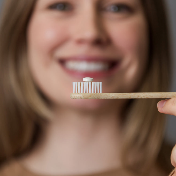 Person holding a toothbrush with a small container on a blurred background