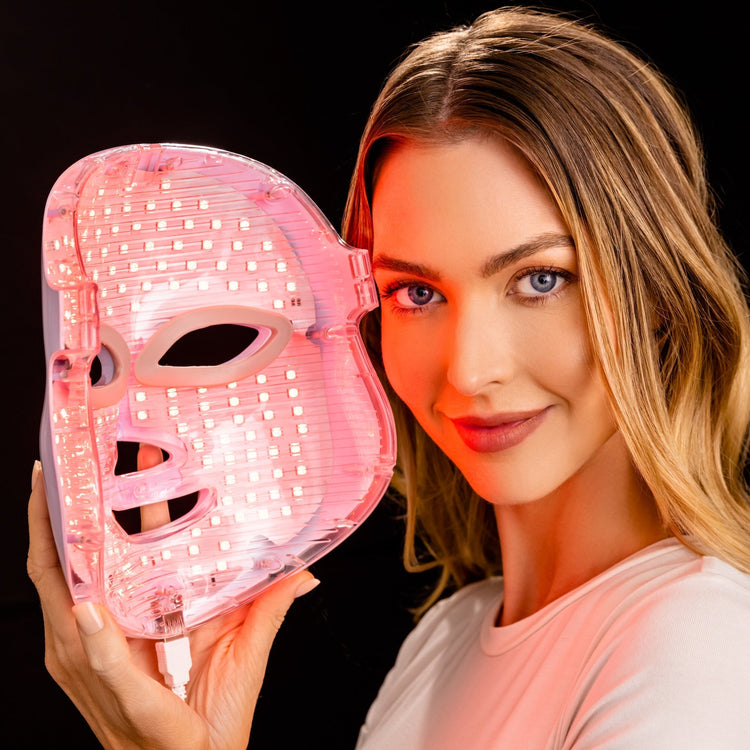 Woman holding a pink LED face mask against a black background