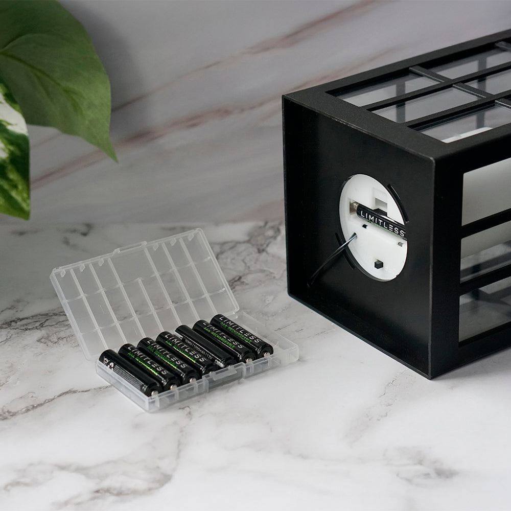 Black clock with a clear container holding batteries on a marble surface.