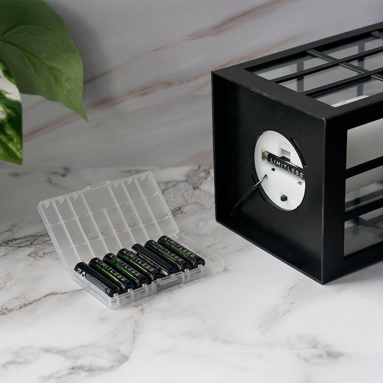 Black clock with a clear container holding batteries on a marble surface.