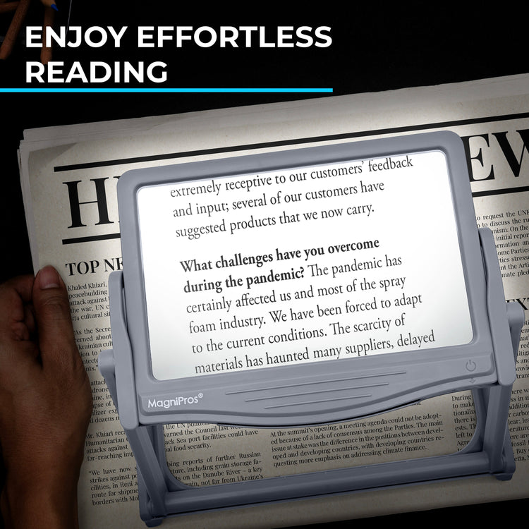 Magnifying device held over a newspaper with text displayed on screen, against a black background.