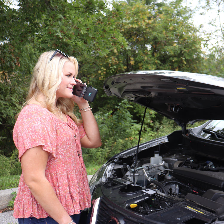 Woman talking on a phone next to an open car hood outdoors