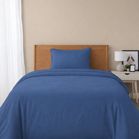 Red bedspread on a wooden bed with a white nightstand and decor items in the background.