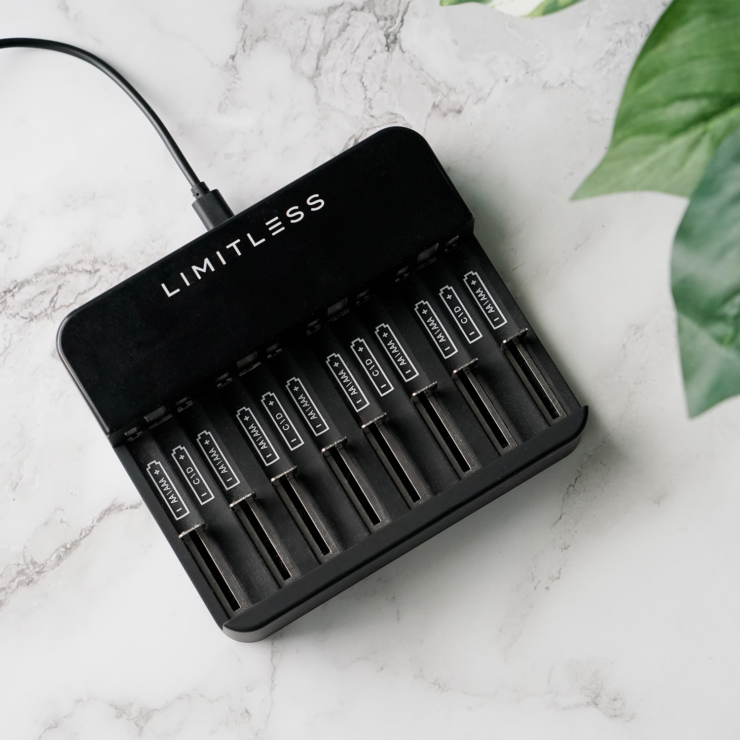 Black battery charger with 'Limitless' branding on a marble surface with green leaves.