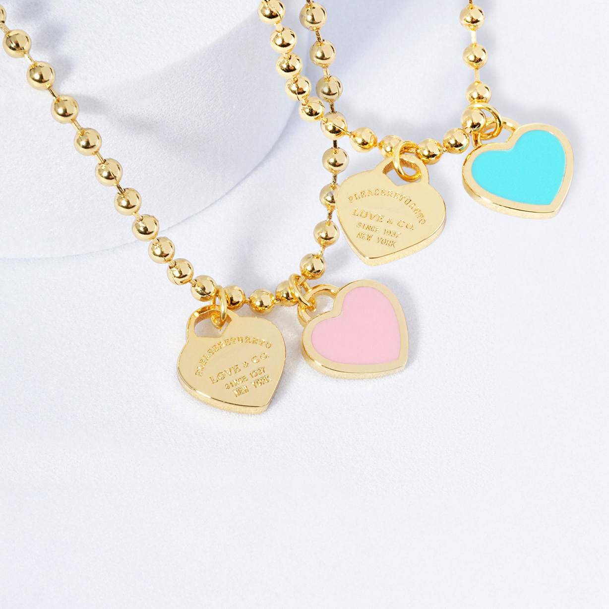 Gold beaded necklace with heart-shaped charms on a white background
