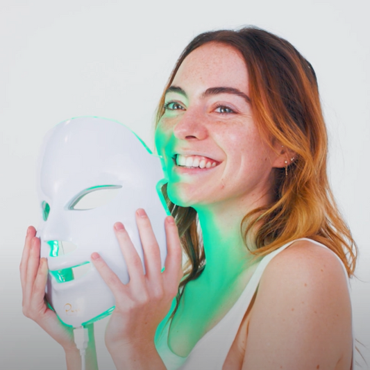 A LED light therapy facial mask and a bottle of high energy hyaluronic serum, both branded by Pure Daily Care, with the mask illustrated in a rainbow of light colors and the serum bottle labeled.