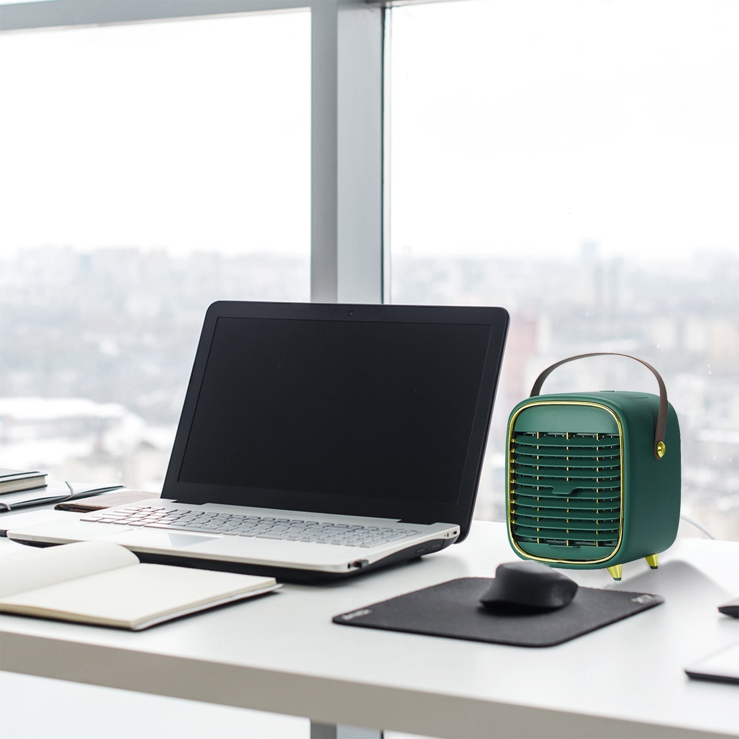 Laptop on a desk with a small green portable air conditioner in an office setting