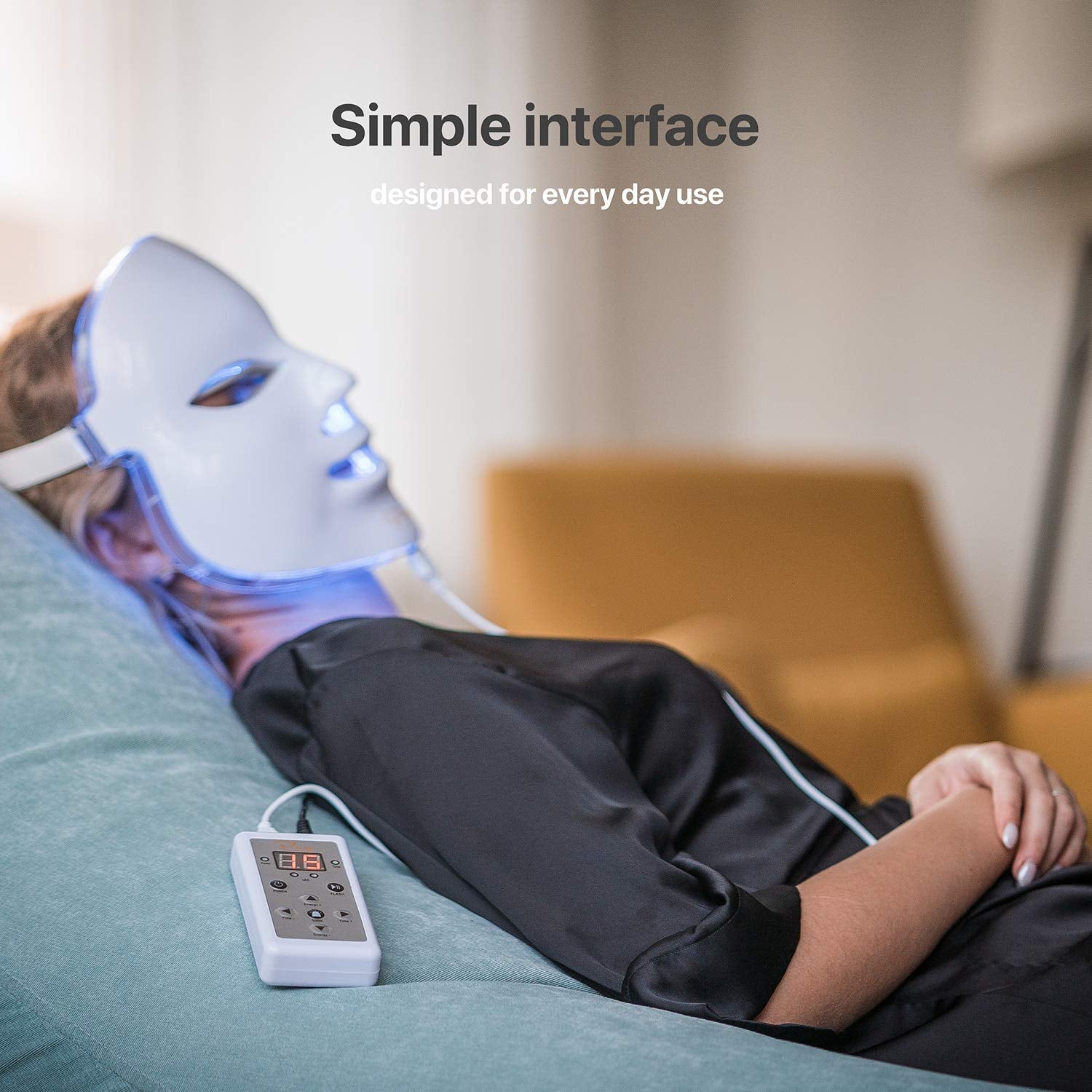 Person wearing a LED face mask with a control device on a couch, text 'Simple interface designed for every day use'.