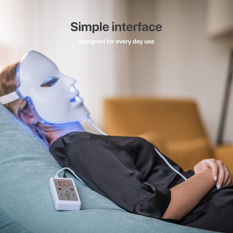 Person wearing a LED face mask with a control device on a couch, text 'Simple interface designed for every day use'.