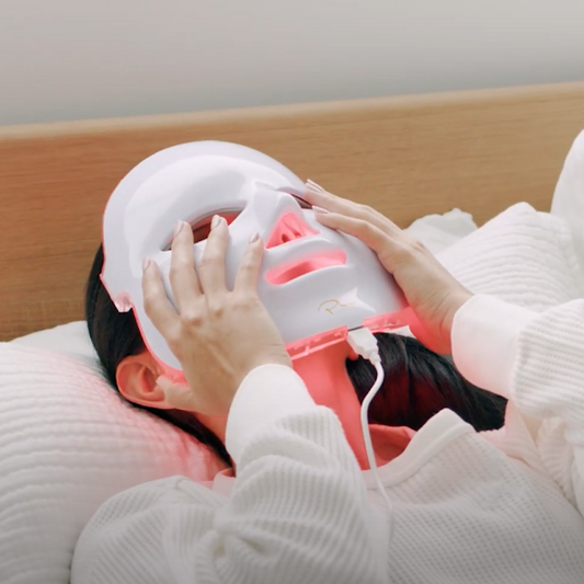 A LED light therapy facial mask and a bottle of high energy hyaluronic serum, both branded by Pure Daily Care, with the mask illustrated in a rainbow of light colors and the serum bottle labeled.