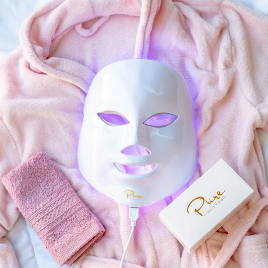 A LED light therapy facial mask and a bottle of high energy hyaluronic serum, both branded by Pure Daily Care, with the mask illustrated in a rainbow of light colors and the serum bottle labeled.