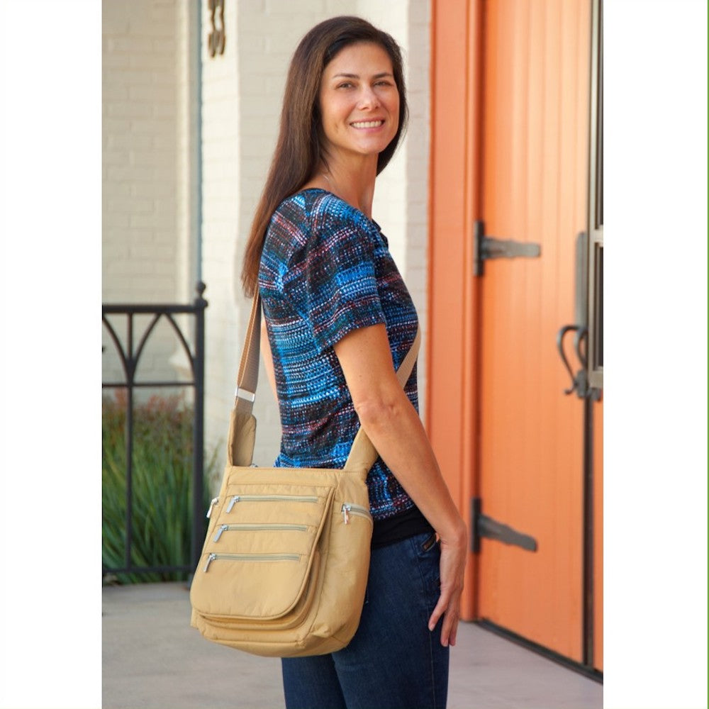 A person smiling and carrying a beige crossbody vegan leather daybag with zippered pockets.