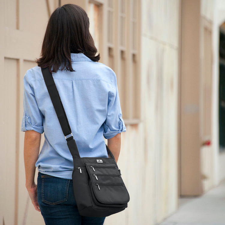 A person walking away from the camera wearing a blue shirt and carrying a black crossbody daybag with shoulder strap.