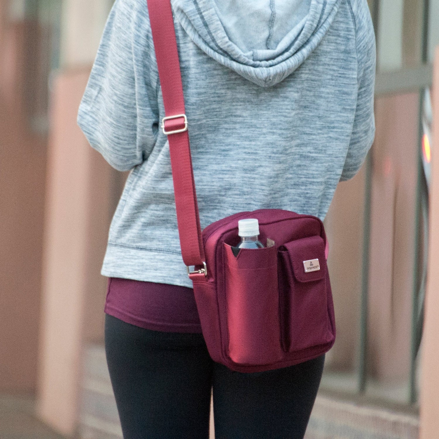 Person wearing a gray hoodie and dark pants with a purple crossbody bag.