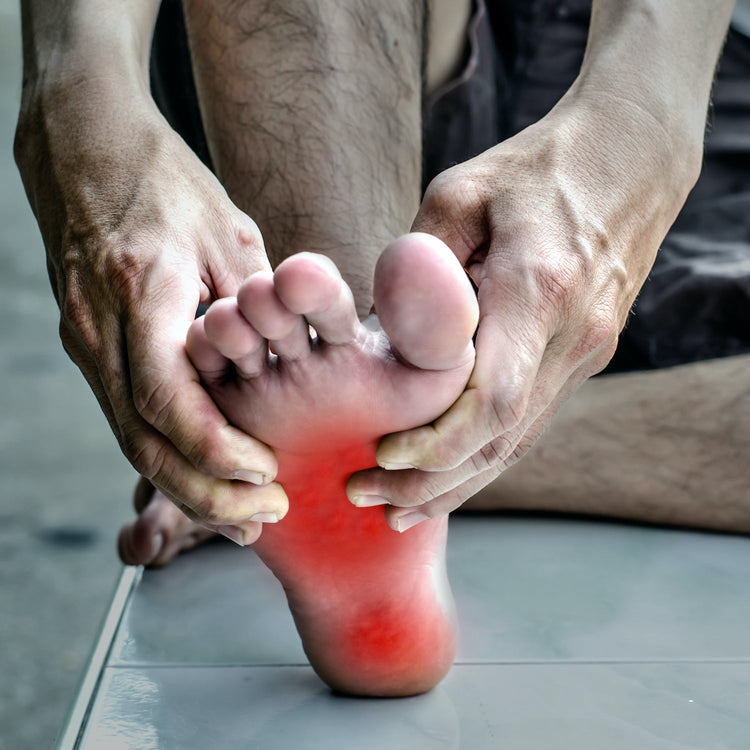 Person holding a painful foot with a red highlight on a tiled floor.