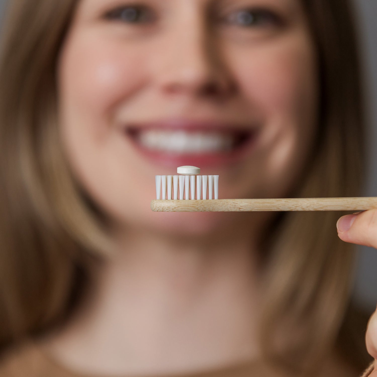 Person holding a toothbrush with a small container on a blurred background