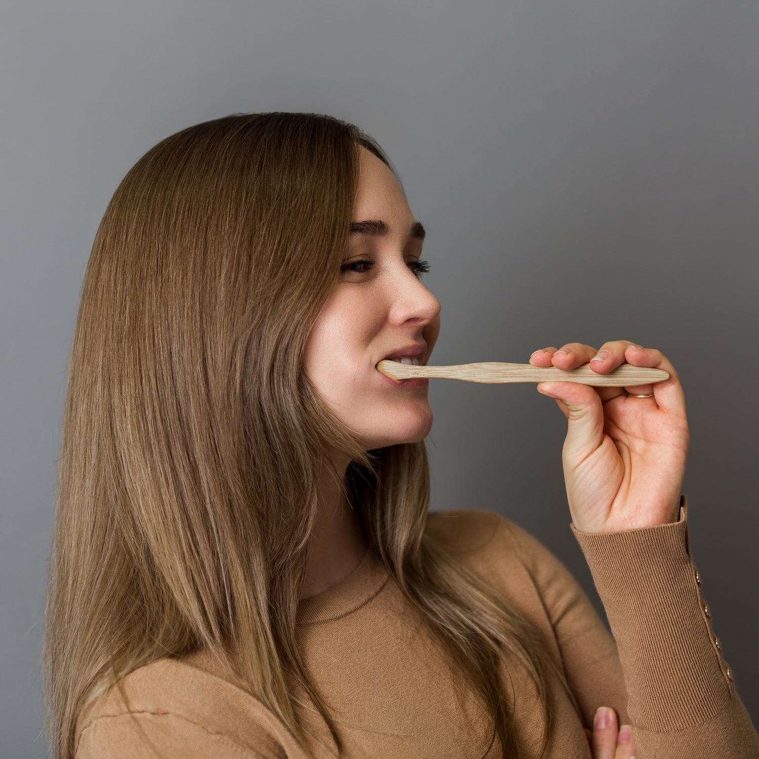 Woman applying cream to her face with a brush against a gray background
