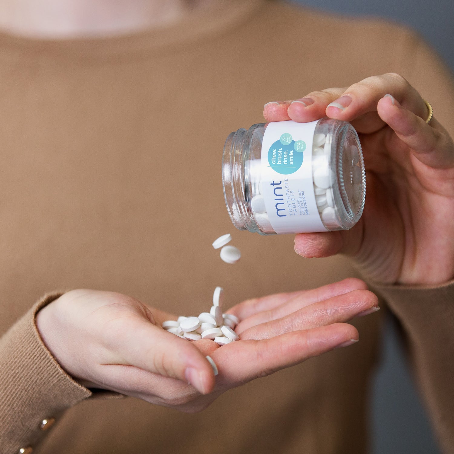 Person holding a jar of white capsules labeled 'mint' with some capsules in their hand.