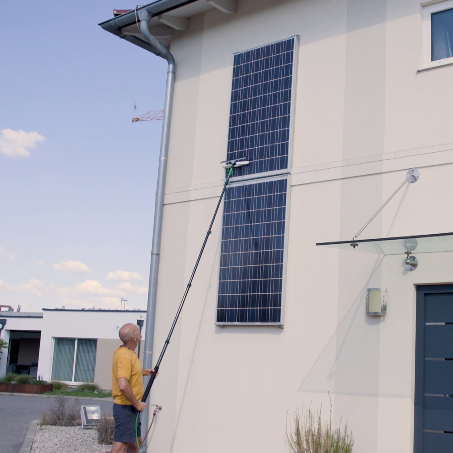 Person cleaning a solar panel on a building with a long pole