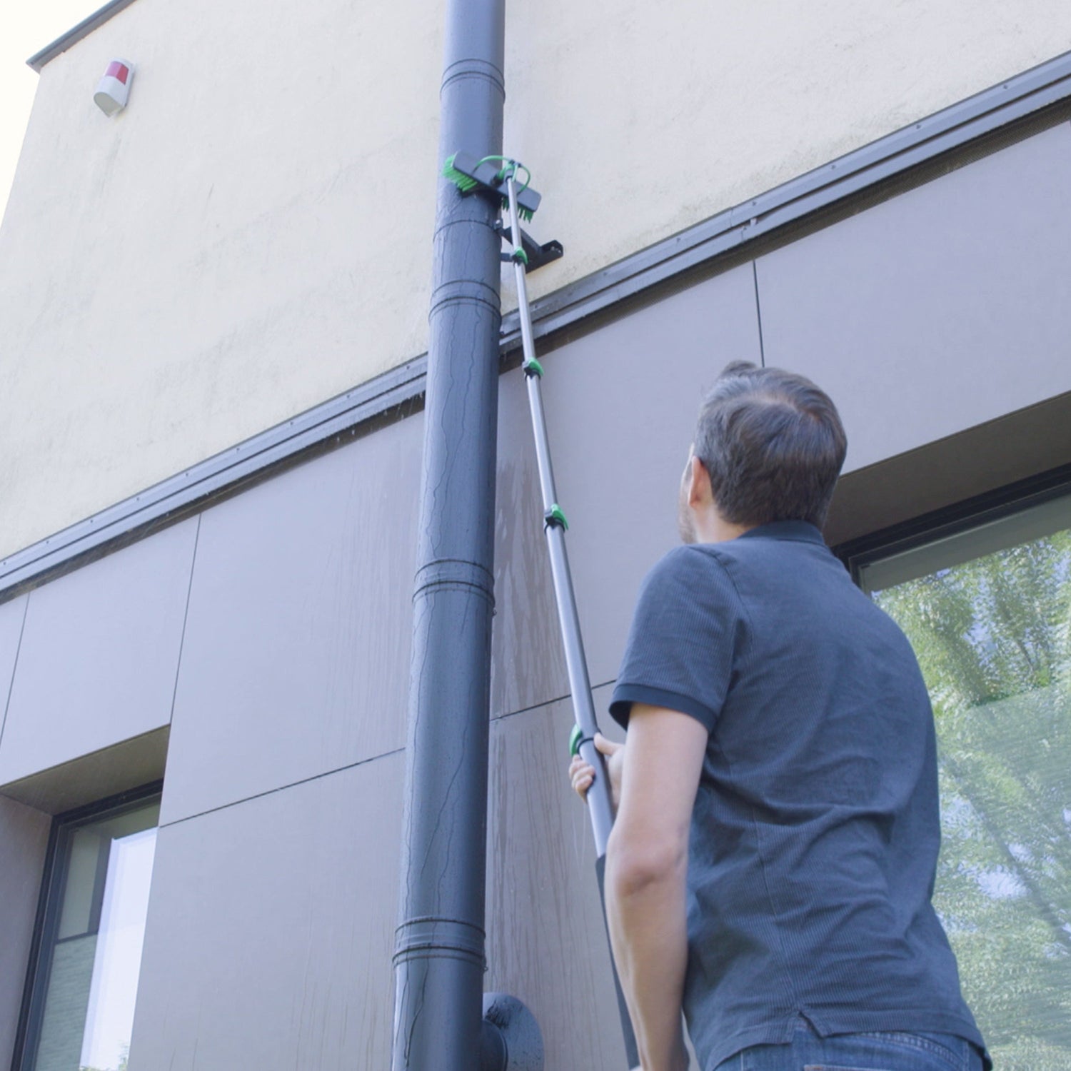 Person using a telescopic cleaning tool on a building exterior