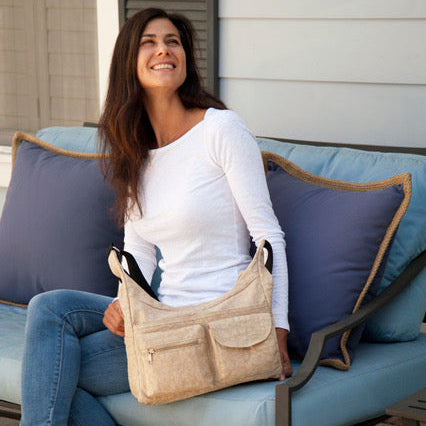 Woman sitting on a patio with a beige handbag, smiling outdoors.