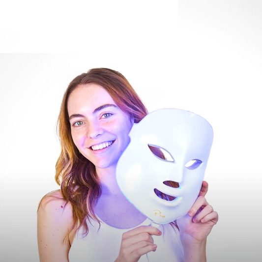 A LED light therapy facial mask and a bottle of high energy hyaluronic serum, both branded by Pure Daily Care, with the mask illustrated in a rainbow of light colors and the serum bottle labeled.
